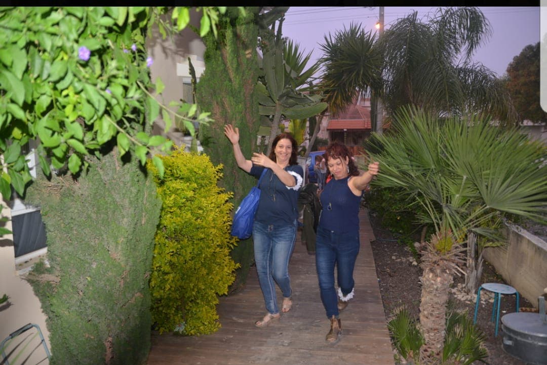 אורחות צוחקות ומנופפות לעבר המצלמה כשהן מגיעות בשביל הגן של לילי בדמדומים