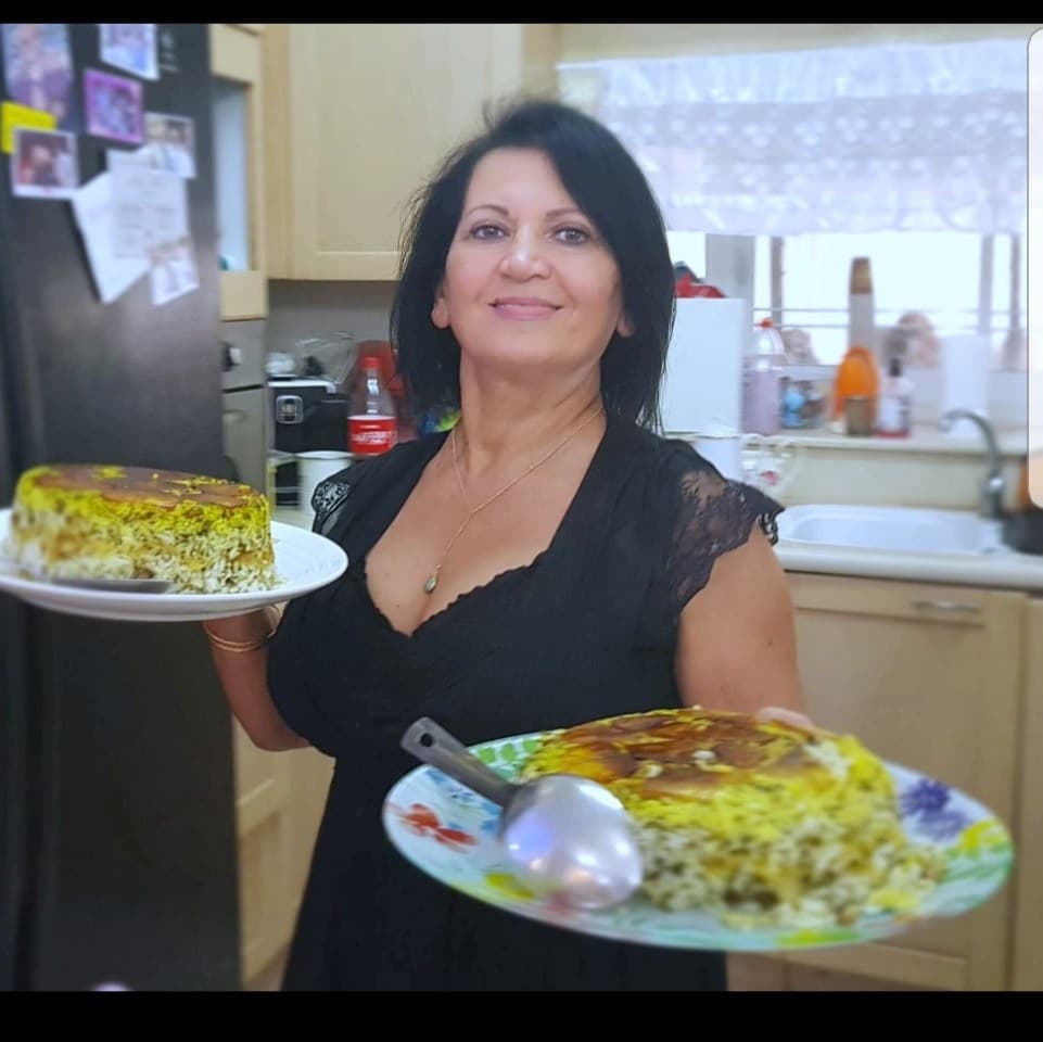 לילי טויזר מחייכת ומחזיקה שני מגשים של אורז פרסי זעפרן עם תחדיג