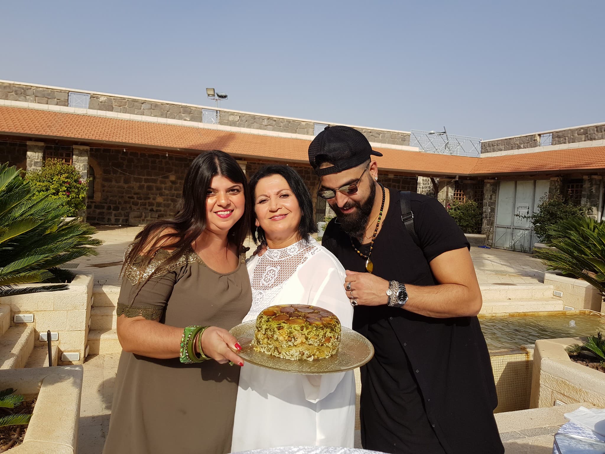 Lili Twizer with guests holding a Persian rice pie in the Beit Shean home courtyard