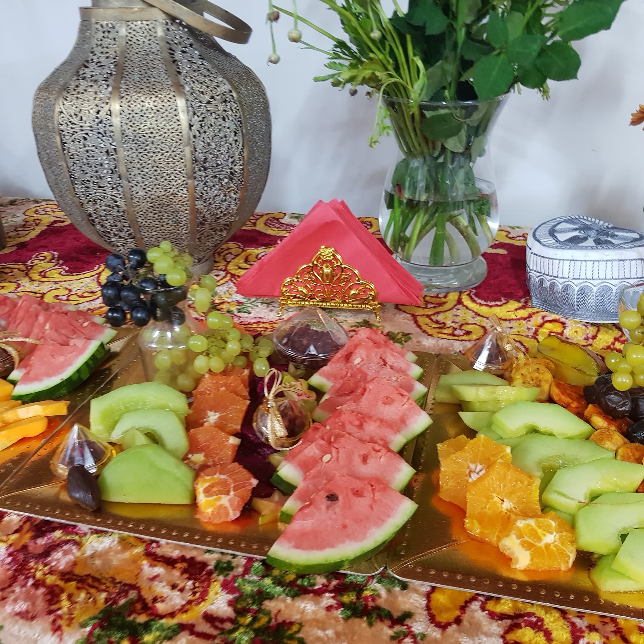 Traditional Persian fruit platter — watermelon, melon and grapes on an embroidered runner beside an ornate brass lantern