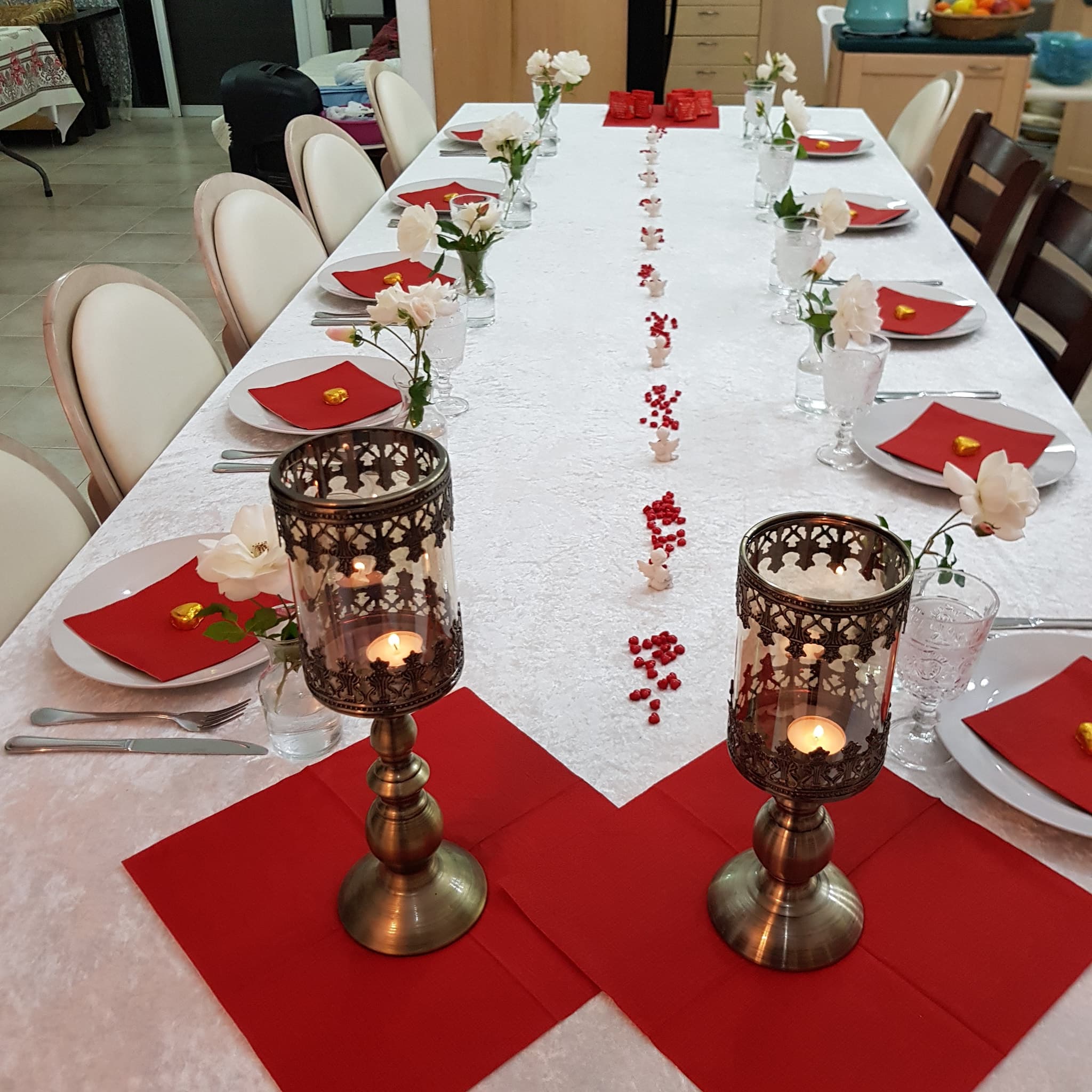 שולחן הפרגולה ערוך לקבלת אורחים עם מפיות אדומות, פרחים לבנים ופנסים מגולפים