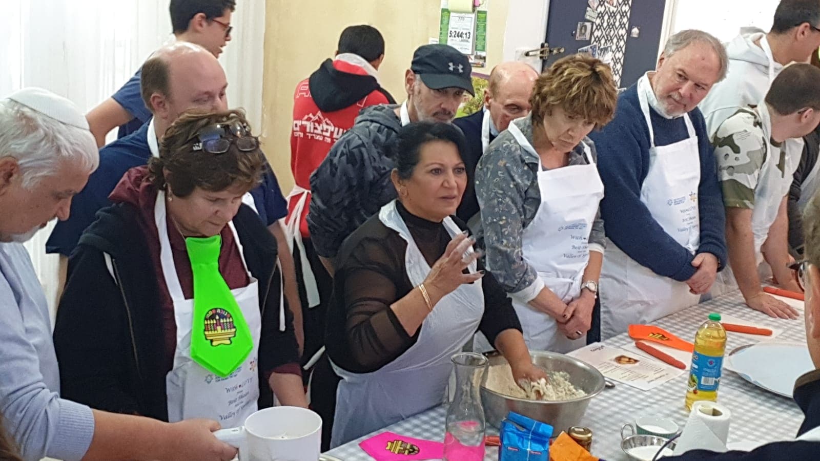 קבוצת אורחים בסדנת בישול עם לילי טויזר — כולם לובשים סינרים ומכינים בצק